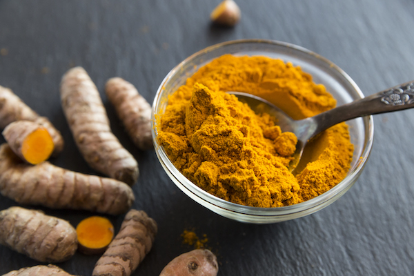 Glass bowl of curcuma powder and fresh organic curcuma on slate